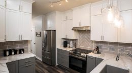 Two Toned Cabinets In Modern Kitchen. White cabinets up top dark grey cabinets with stainless steel hardware. White and grey marbled countertops. Grey Subway Tile Backsplash.